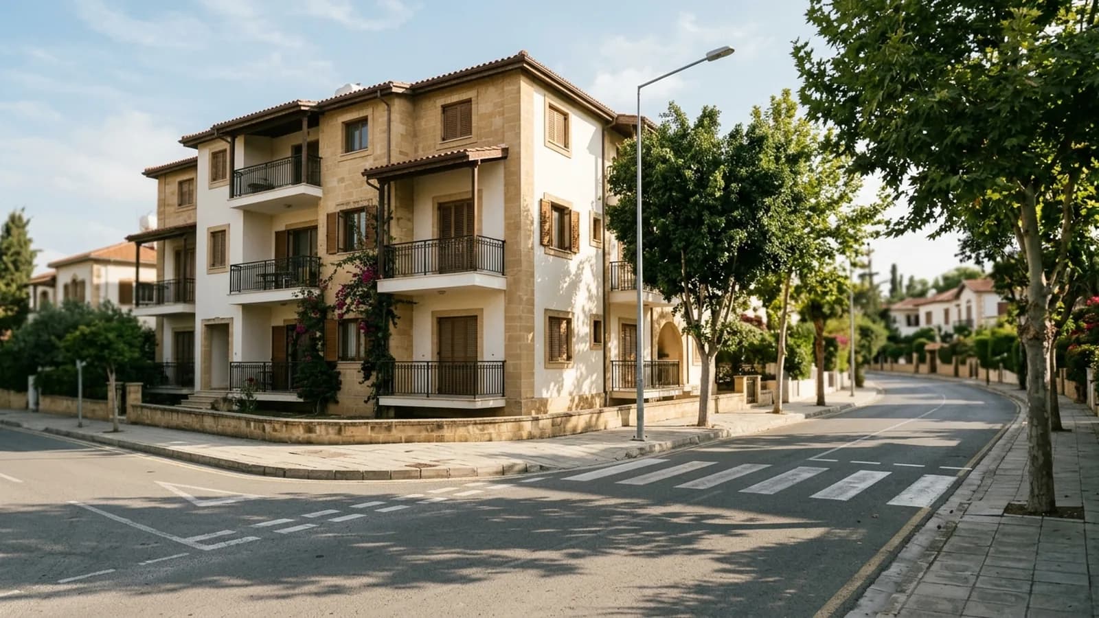 Sakin bir banliyö sokak köşesi: gölgeli balkonları olan alçak apartman, kesintisiz kaldırım, aydınlatma direği ve asfalttaki yaya geçidi — temsili görsel