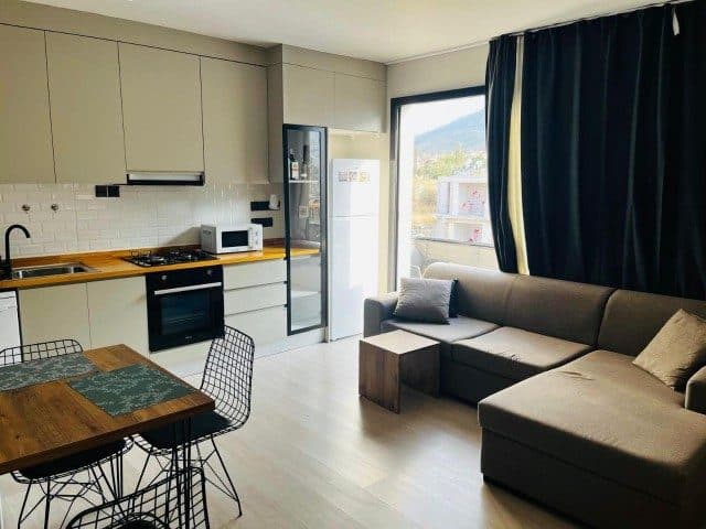 Açık mutfak, ahşap masa ve köşe koltuk balkon kapısının yanında