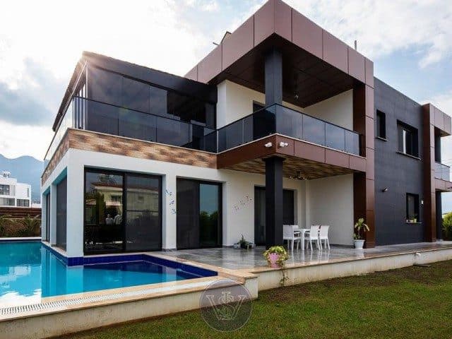 The facade with glass balcony overlooks a pool and paved terrace.