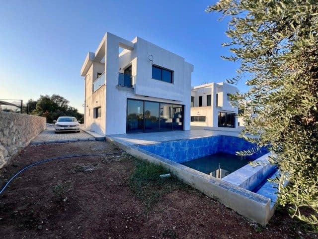 Beyaz cepheli villa, mavi havuz ve toprak bahçeyle görünüyor
