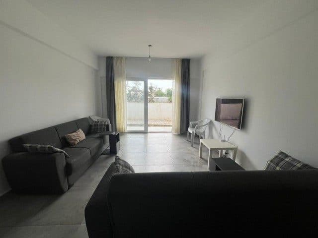 Koyu renk koltuklar, duvar televizyonu ve sürgülü balkon kapısı