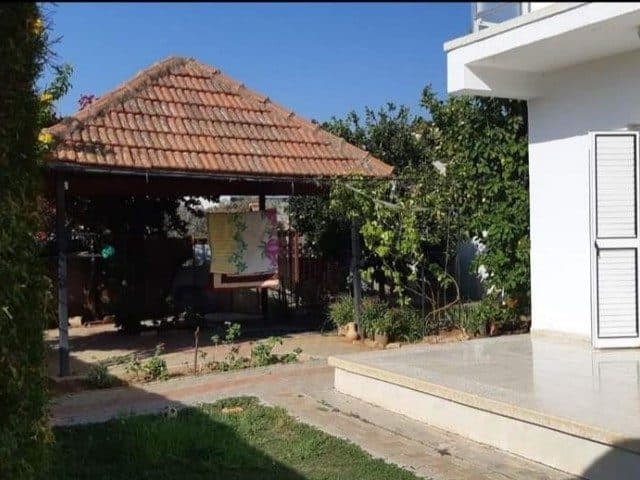 Çim ve ağaçların yanında kiremit çatılı ahşap kamelya