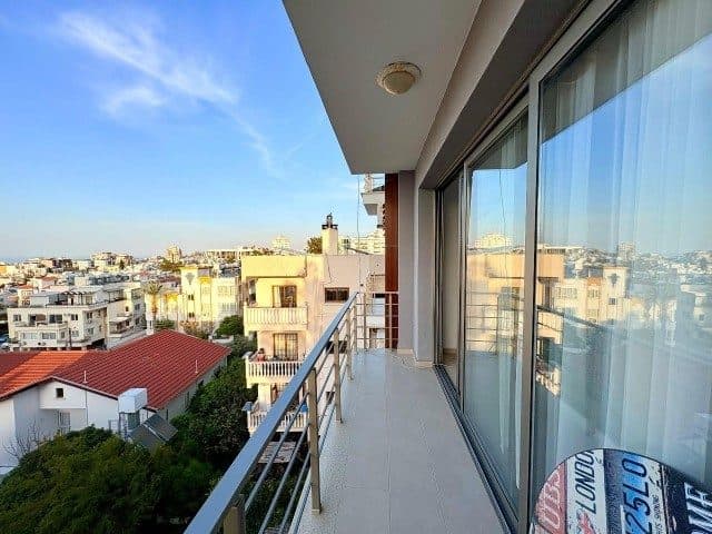 Cam kapılı balkon, metal korkuluk ve çevredeki binalara bakıyor.