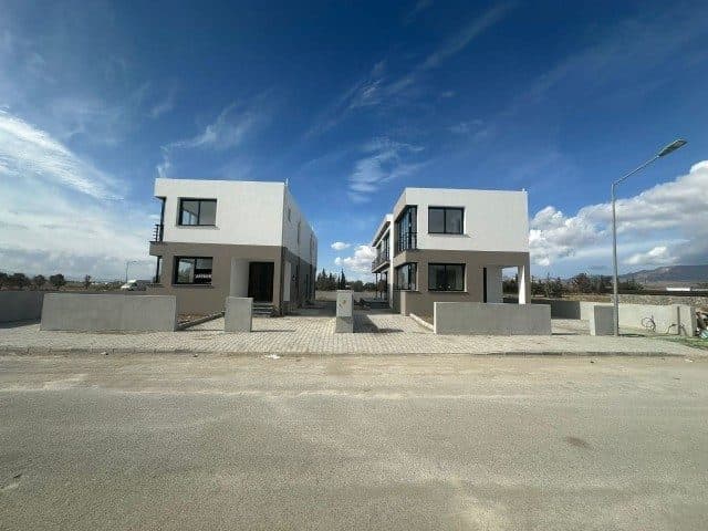 İki modern ev, alçak duvarlı ön alan ve taş döşemeli girişle görülüyor.