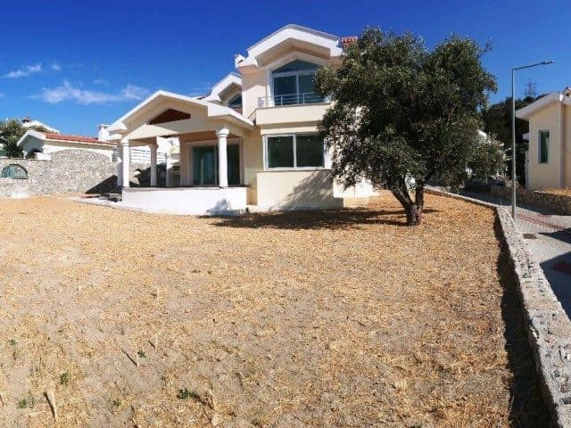 Açık renkli cephe, üst balkon ve kuru çimlerle çevrili bahçe