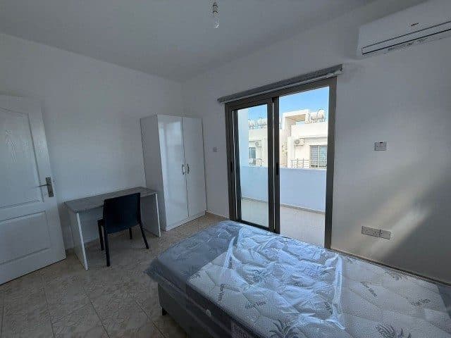 Yatak, çalışma masası ve sürgülü kapıdan görünen balkon
