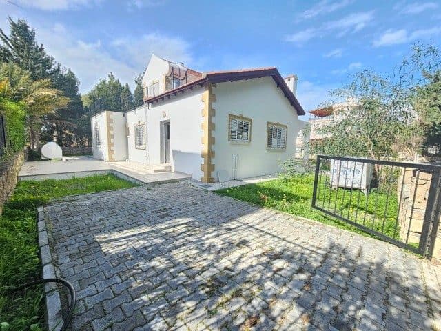 Taş döşeli araç girişinden beyaz cephe ve panjurlu pencereler görünüyor.