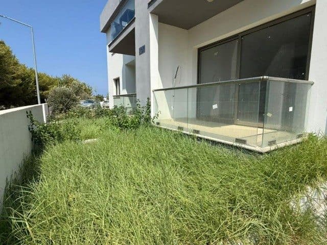 Cam korkuluklu balkonun önünde uzun otlarla kaplı bahçe