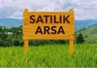 Yeşil arazide satılık arsa tabelası, arkada tepeler görünüyor
