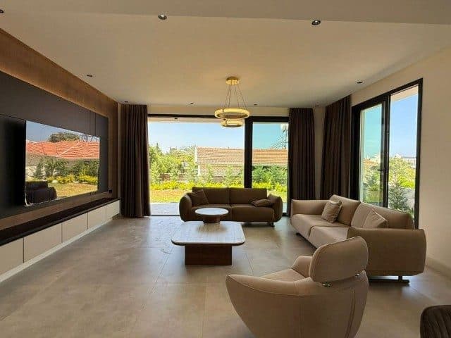 Bej koltuklar, orta sehpalar ve geniş camlı salon