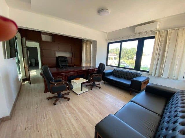 Dark wood desk, black sofas, and wide windows