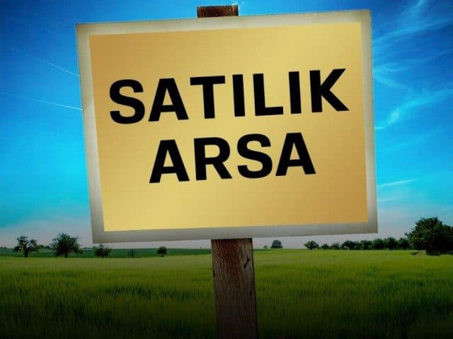 Yeşil arazi önündeki tabelada “Satılık Arsa” yazıyor