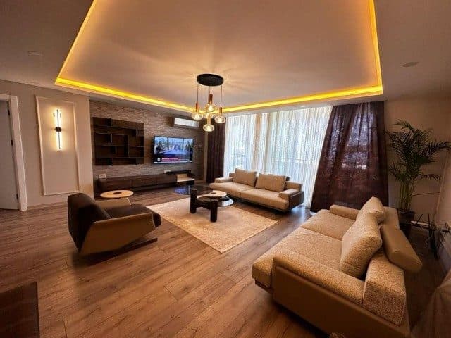 Bej koltuklar, TV ünitesi ve ışık bantlı tavan