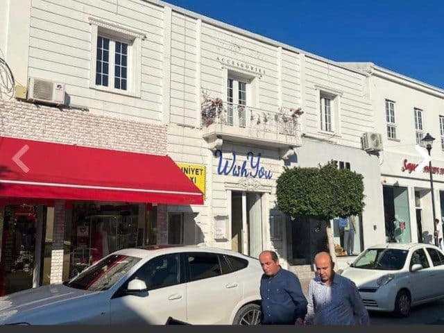 Kırmızı tenteli dükkân cephesi ve kaldırım kenarındaki araçlar