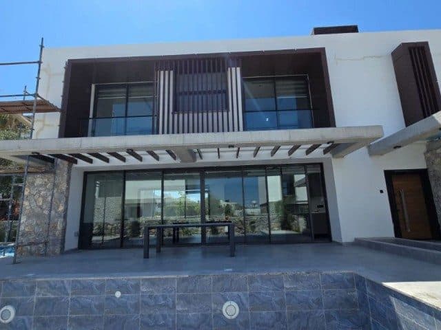 Cam cepheli villa, üst balkon ve taş kaplı havuz alanıyla görünüyor.