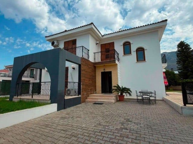 Beyaz cephede ahşap paneller, üst balkon ve taş döşeli giriş