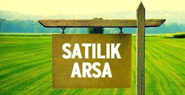 Düz, yeşil arazi önünde dağ silueti ve satılık arsa tabelası