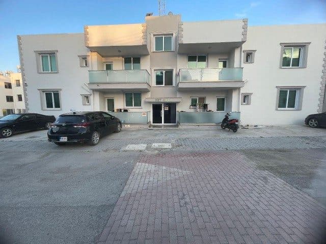 Önden görünen apartman cephesi, cam balkonlar ve giriş önü park alanı