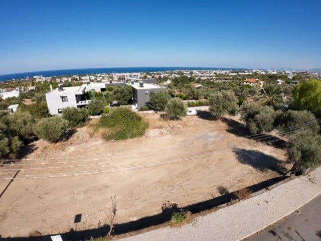 Ön planda boş arsa, arkasında yapılaşma ve deniz görünüyor