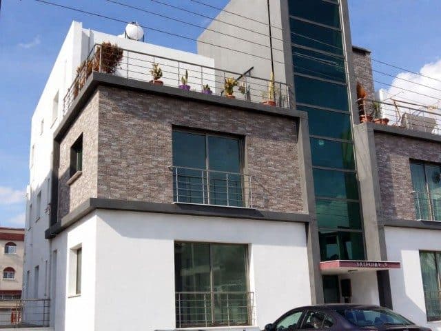 Taş kaplamalı cephede cam korkuluklu balkonlar görülüyor.