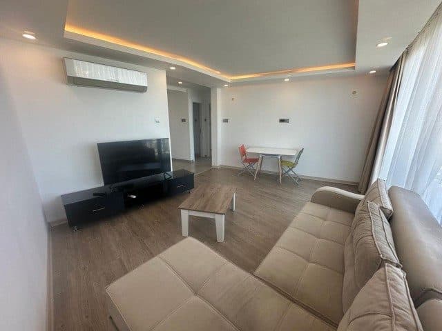 Bej koltuk, televizyon ve yemek masası aynı alanda