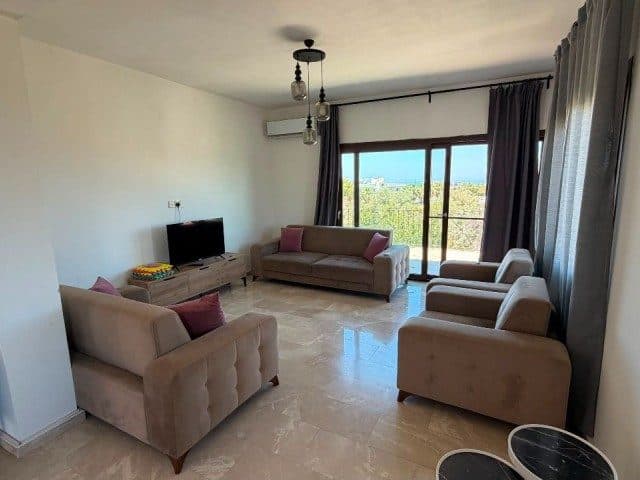Koltuklarla düzenlenmiş salon, cam kapıdan deniz görünüyor.