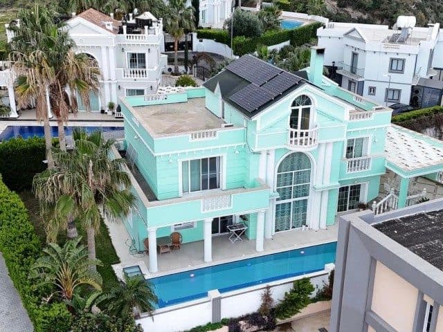 Turkuaz cepheli villa, çatı panelleri ve havuzuyla görünüyor.