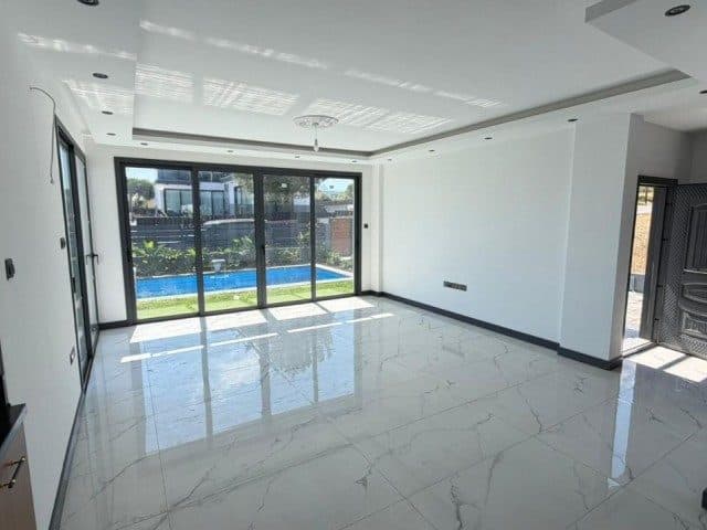 Boş, parlak fayanslı salon; sürgülü camlardan havuz görünüyor