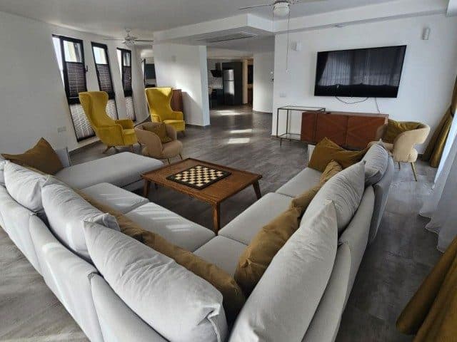 A gray corner sofa, yellow armchairs, and TV unit share the space.