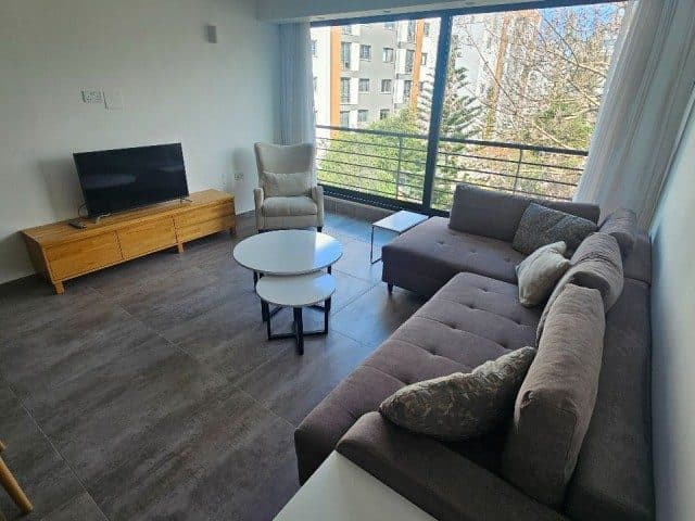 Gri köşe koltuk, televizyon ve geniş camlı balkon görünümü