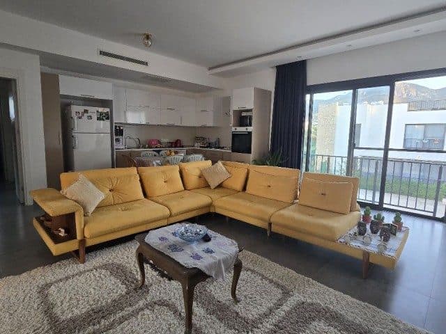 Sarı köşe koltuk, desenli halı ve açık mutfak balkon kapısına bakıyor