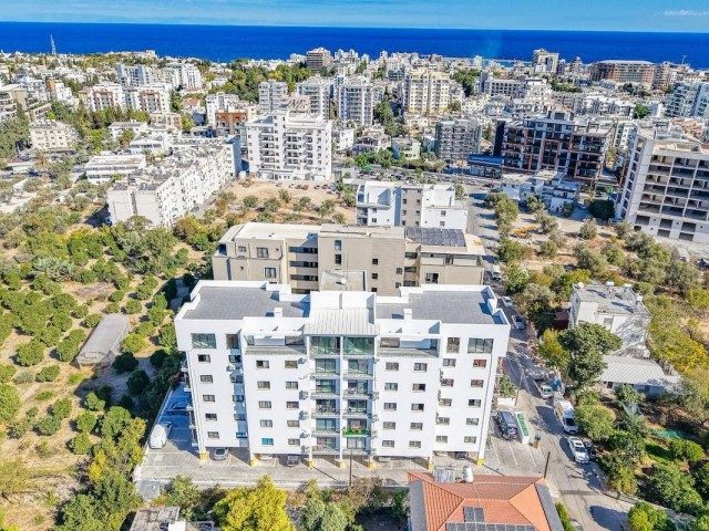 Apartman cephesinin önünde yoğun yapılaşma ve uzakta deniz görünüyor