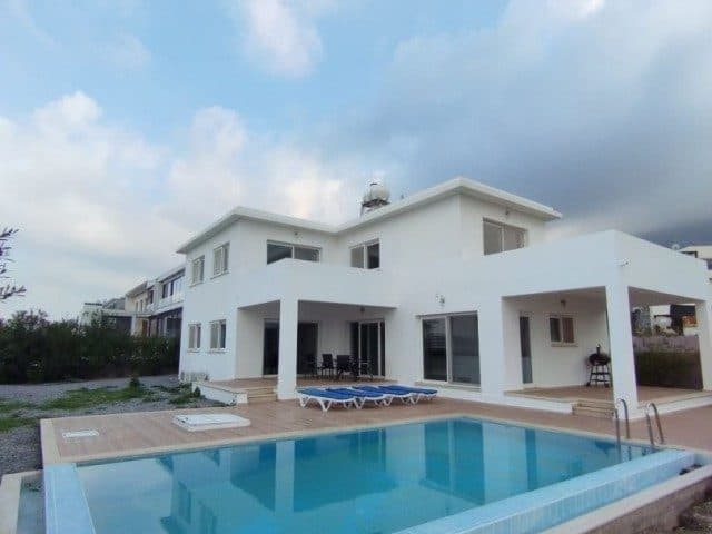 Beyaz villanın önünde mavi havuz ve ahşap görünümlü teras