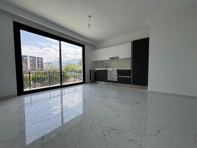 Boş salon, açık mutfak ve dağlara bakan sürgülü balkon kapısı