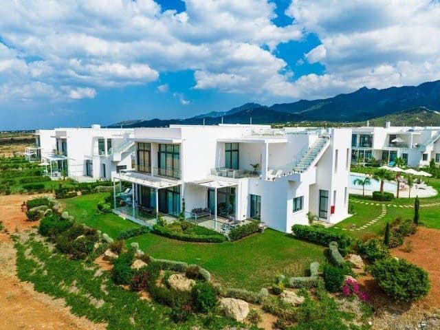 Beyaz cepheli daireler, peyzajlı bahçe ve dağ sırtı önünde