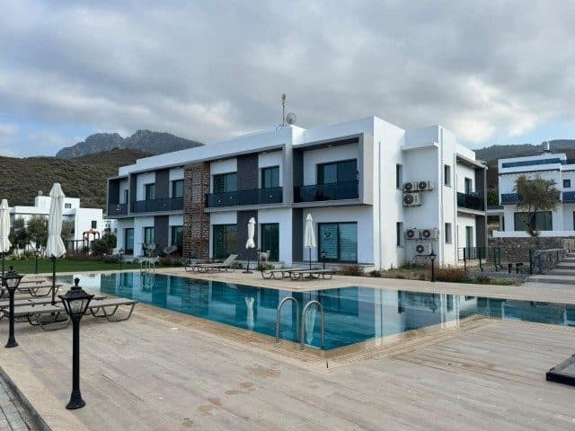 Havuz kenarında koyu balkon korkuluklu beyaz apartman bloğu