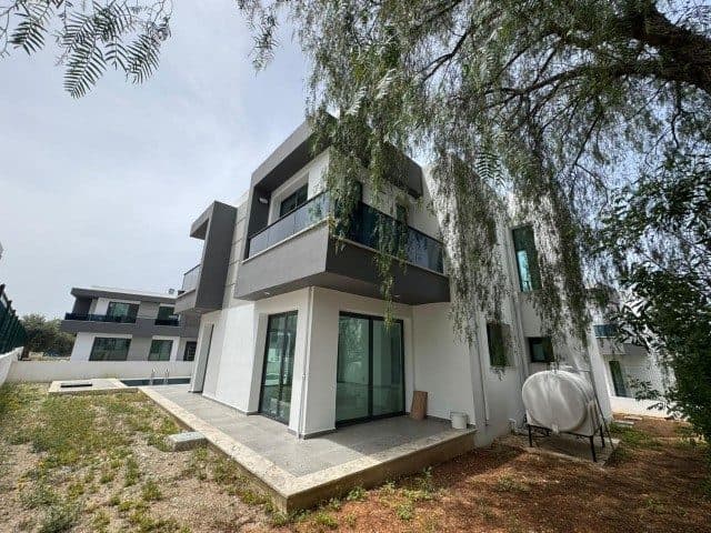 Beyaz ve gri cepheli ev, cam balkon ve küçük bahçeyle çevrili