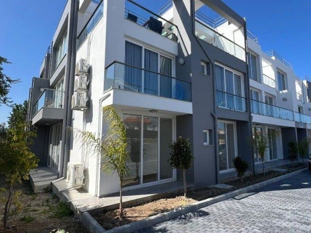 Gri-beyaz cephe, cam balkonlar ve giriş önündeki küçük peyzaj alanı