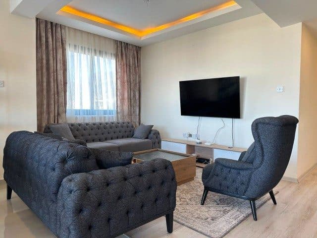 Koyu koltuklar, duvar tipi TV ve pencere önünde perde