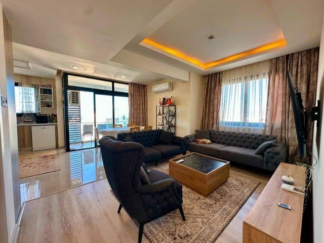 Koyu renkli koltuklar, ahşap sehpa ve sürgülü balkon kapısı