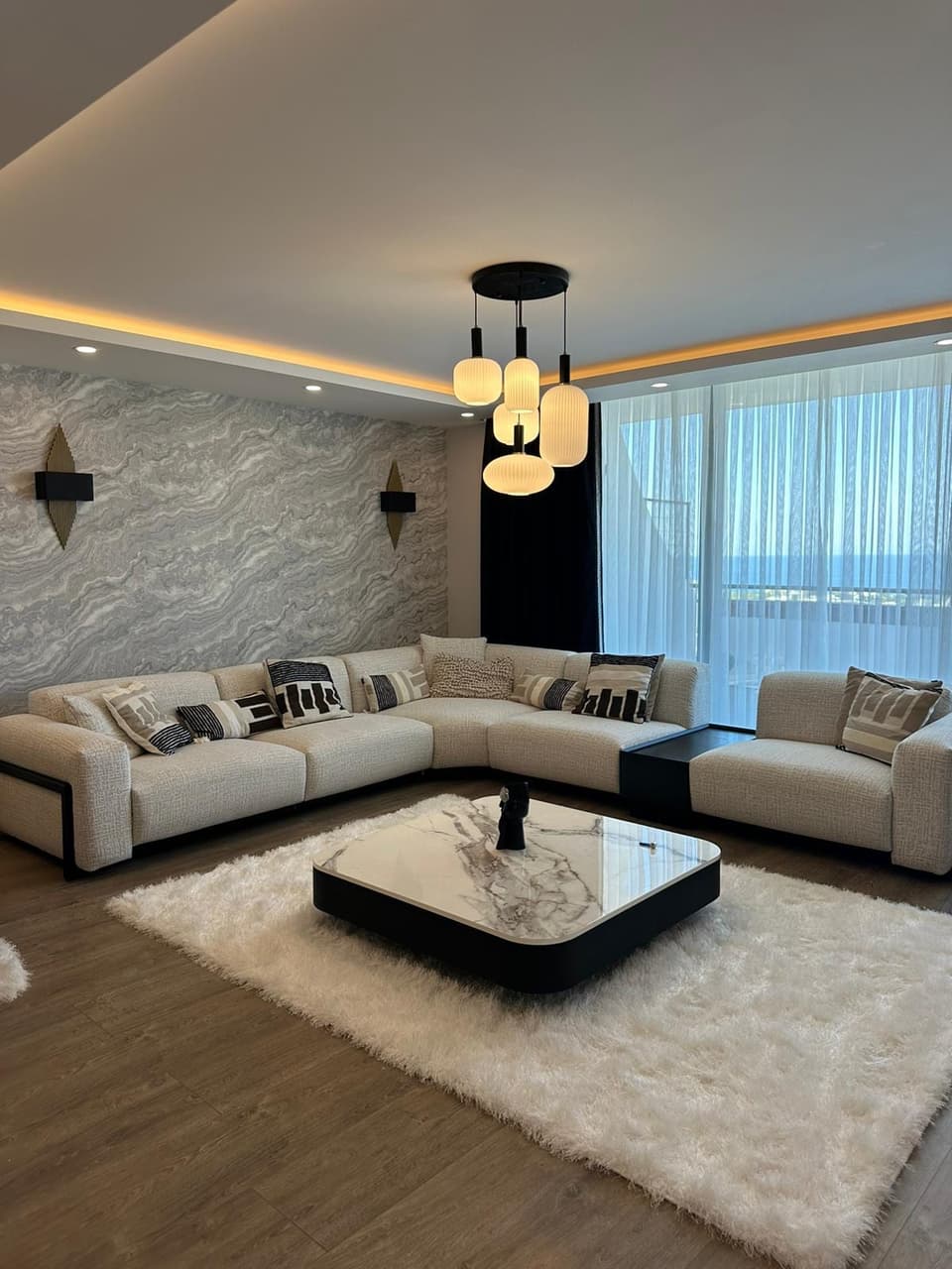 Geniş pencereli, modern mobilyalı salon ve deniz manzarası.