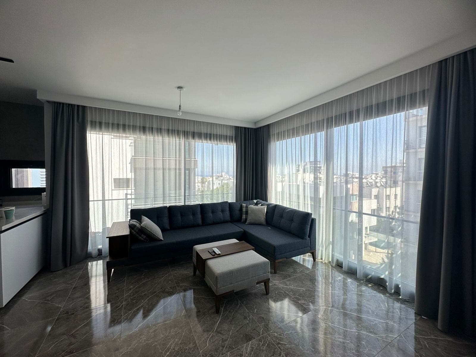Living area with modern corner sofa, large windows, and city view.