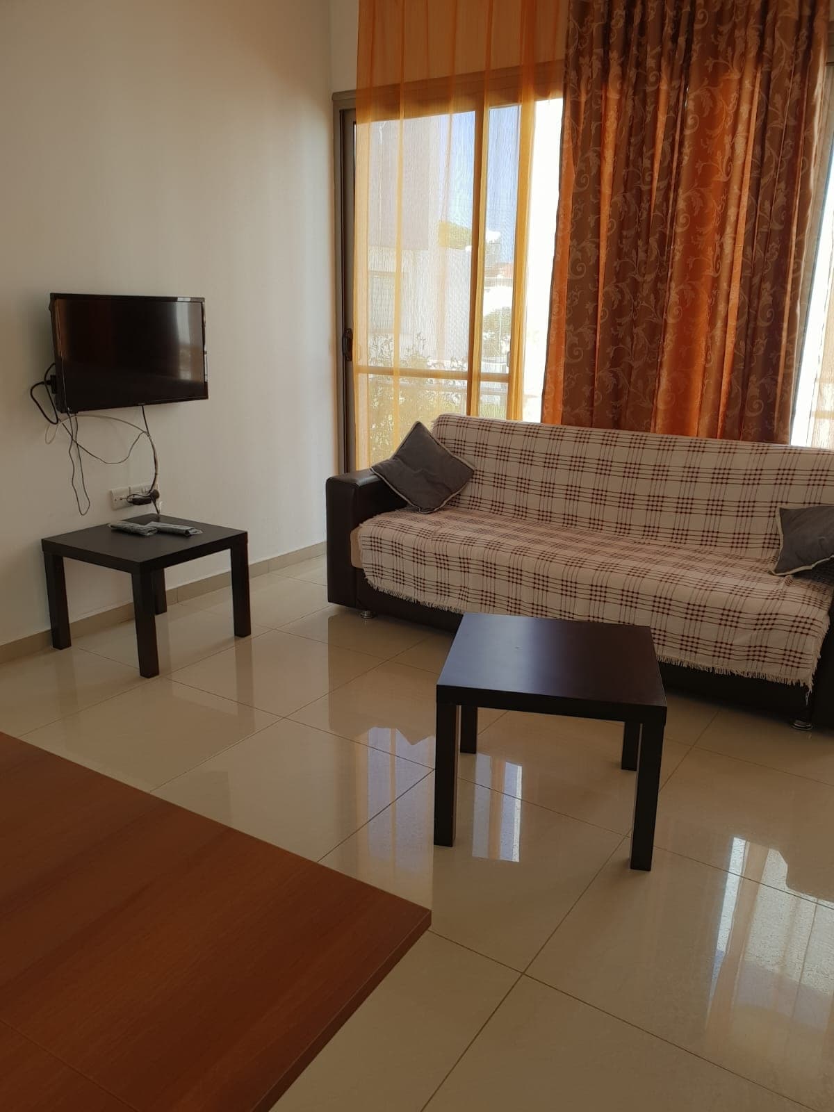 Living room with a checked sofa cover, wall-mounted TV and orange curtains.