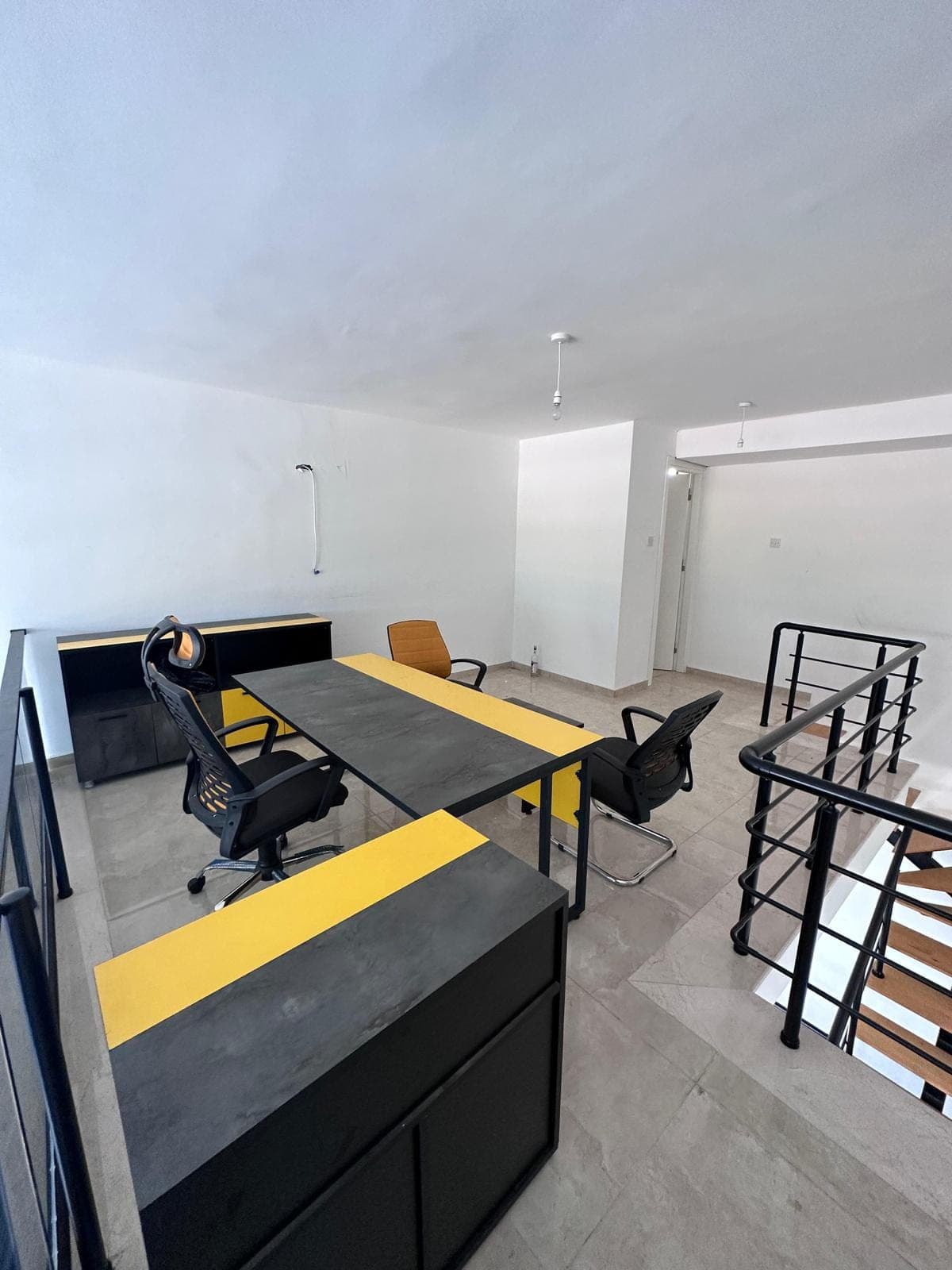 Office desks and chairs with yellow details, looking down from the upper floor.