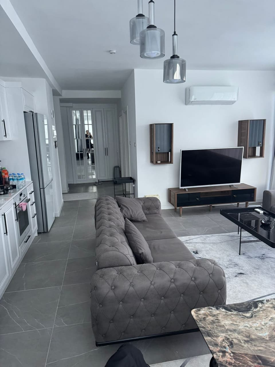 Açık plan salon ve mutfak, gri koltuk takımı ve TV ünitesi.
