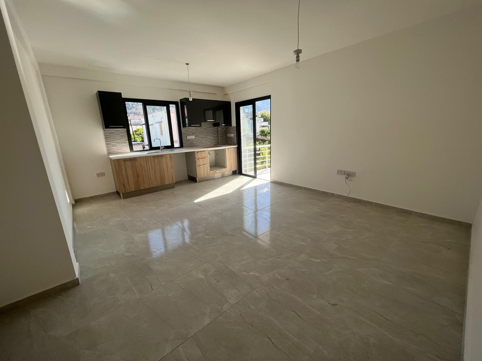 Open-plan kitchen and living area with tiled floor, balcony door.