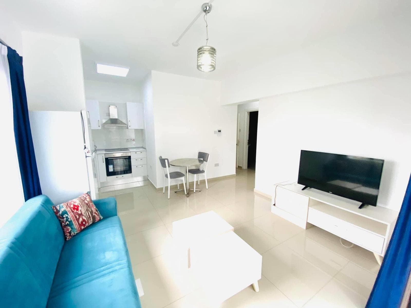 Open-plan living room and kitchen with blue sofa and TV unit.