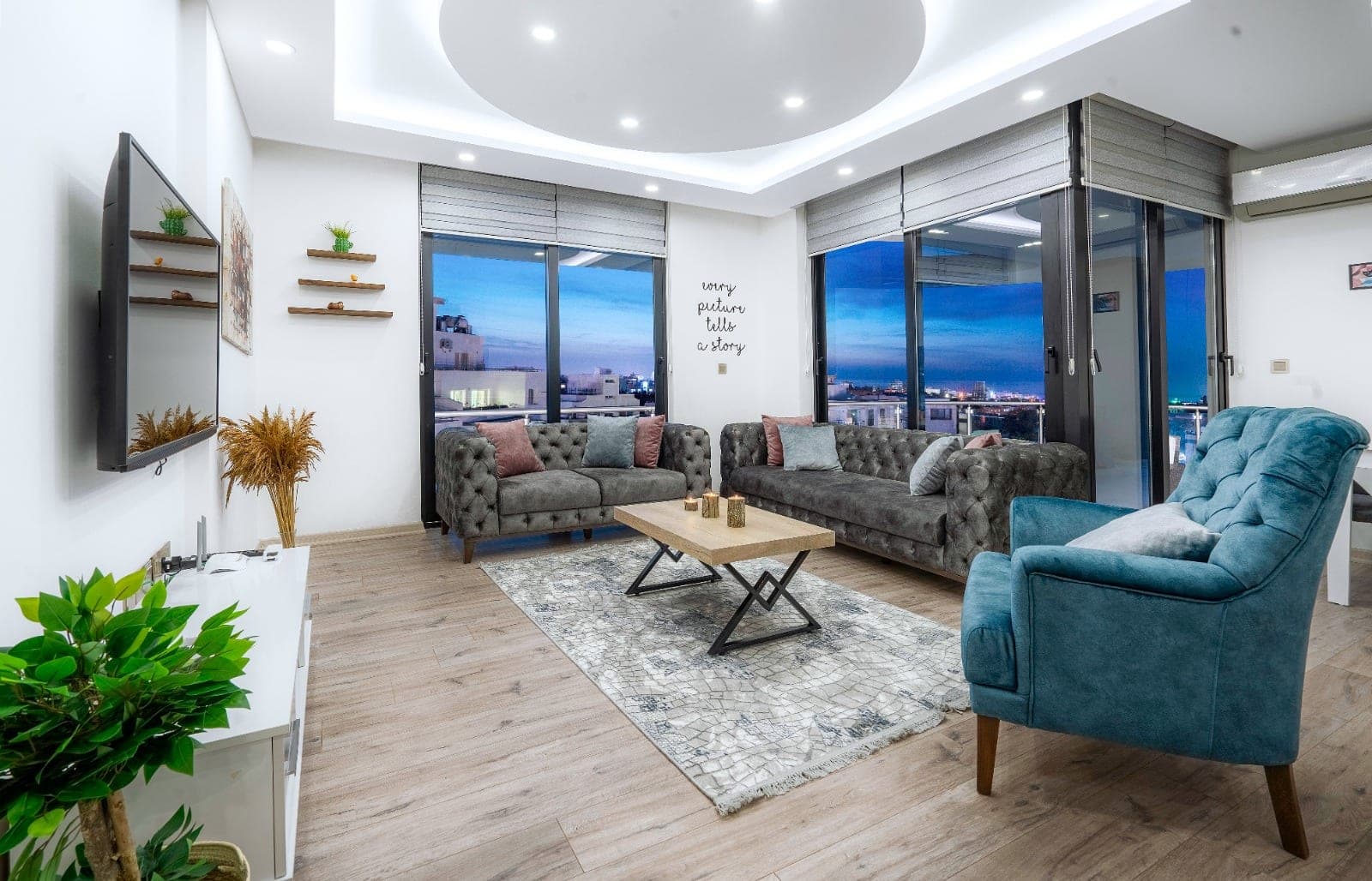 Modern mobilyalı salon, geniş pencerelerden şehir manzarası ve balkon erişimi.