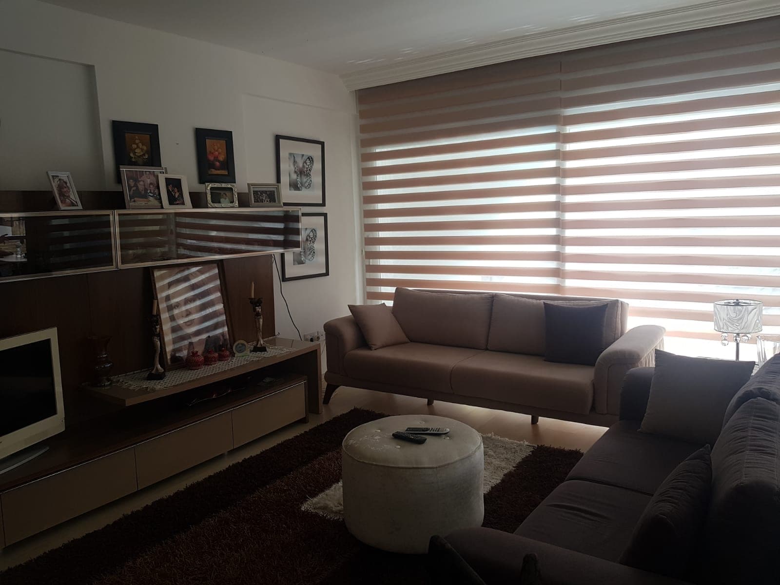 Living room with large windows, brown sofa set, and TV unit.