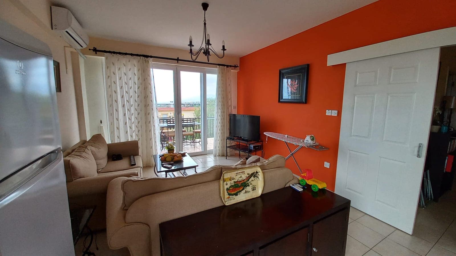Living room with orange wall, refrigerator, air conditioning, and balcony view